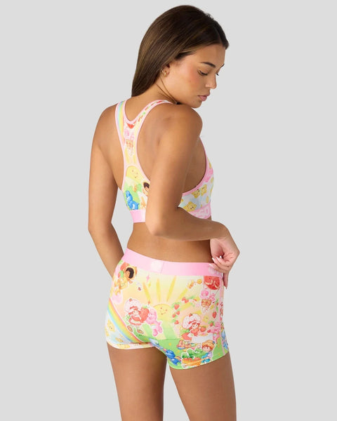 Woman wearing pink and yellow Strawberry Shortcake and Care Bears print sports bra and shorts set, shown from back.