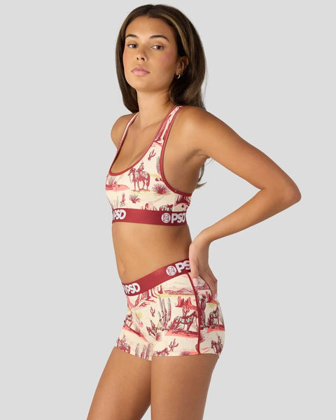 Woman wearing cream and red ranch-themed sports bra and shorts with cattle and cactus print and branded waistband.