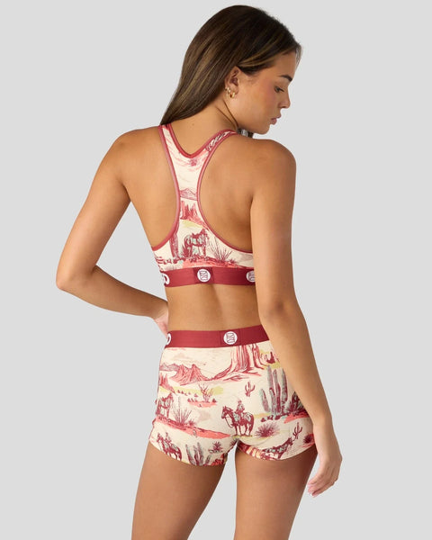 Woman wearing red and cream western-print racerback sports bra and matching shorts with snap details.