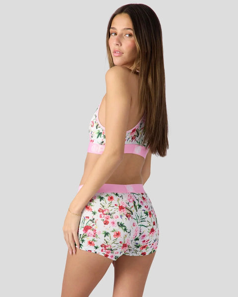 Woman wearing floral patterned sports bra and shorts set with pink trim and white background.