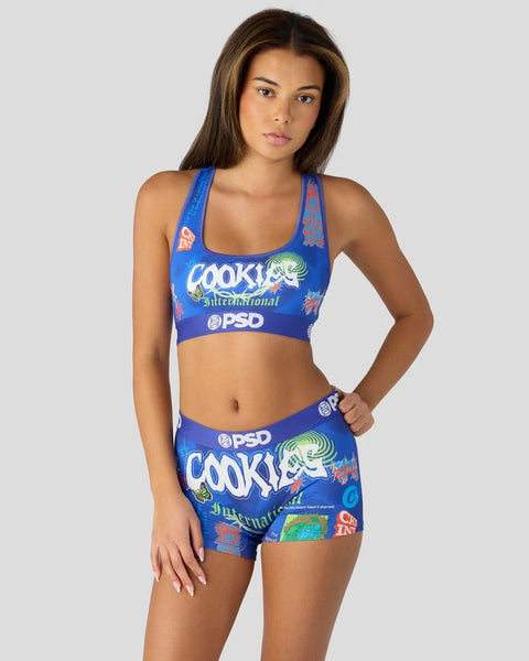 Woman wearing blue Cookies International PSD sports bra and matching shorts with multicolored graphic print.