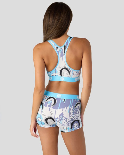 Woman wearing blue sports bra and matching shorts with abstract eye and face print pattern.