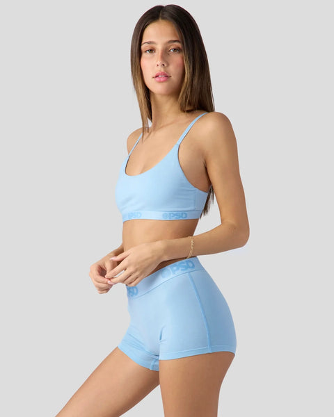 Woman wearing baby blue sports bra and shorts set with thin straps and visible waistband branding.