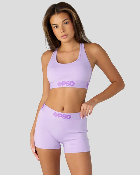 Woman wearing lavender sports bra and matching shorts with branded waistband detail.