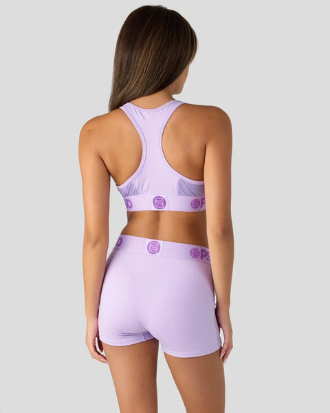 Woman wearing lavender racerback sports bra and matching shorts with purple logo details, shown from back view.