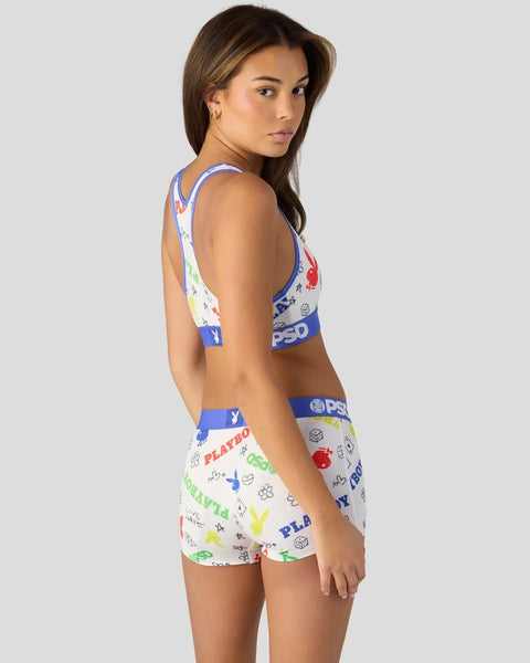 Woman wearing white Playboy-branded sports bra and shorts with multicolored logo print and blue elastic bands.