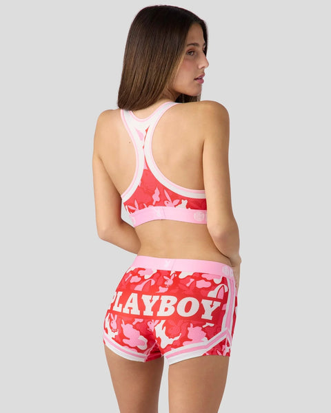 Woman wearing pink and red camouflage sports bra and shorts set with Playboy branding.