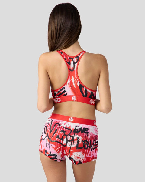 Woman wearing red racer-back sports bra and matching shorts with black and pink graffiti-style print.