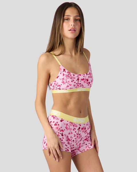 Pink floral crop top and shorts set with yellow trim on model against gray background.