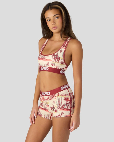 Woman wearing cream and burgundy ranch-themed sports bra and shorts set with desert landscape print and branded waistbands.