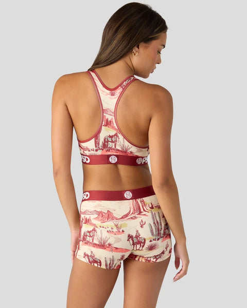 Woman wearing a red and cream ranch-themed sports bra and shorts set with western landscape print and decorative buttons.
