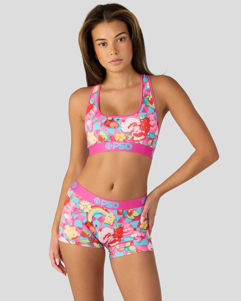 Woman wearing colorful Strawberry Shortcake and Care Bears print sports bra and shorts set with pink elastic bands.