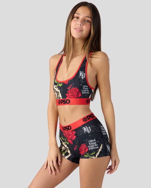 Woman wearing black sports bra and shorts with red roses, text graphics, and red PSD waistbands.