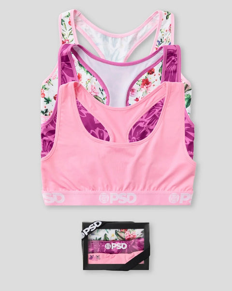 Three sleeveless sports bras in pink, purple, and floral print with branded waistband, shown stacked and packaged in black bo