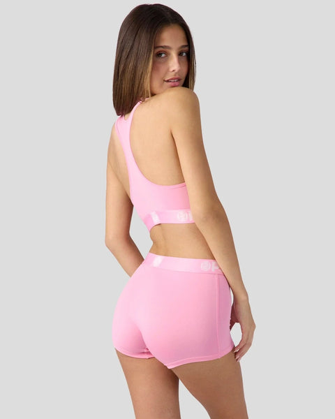 Woman wearing pink sports bra and matching shorts with open back design.