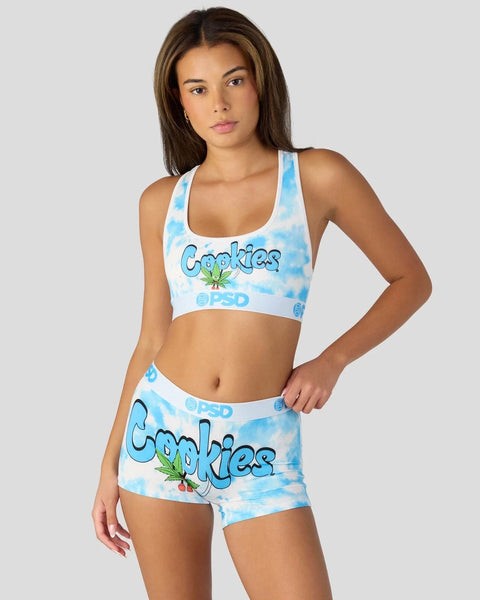Woman wearing a blue and white tie-dye "Cookies" branded sports bra and matching shorts set.