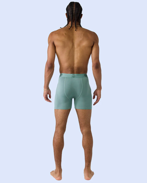 Man wearing sage green boxer briefs with square logo waistband, shown from behind against light blue background.