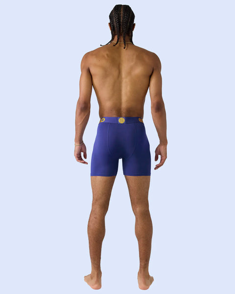 Man wearing royal blue boxer briefs with gold button detail, shown from behind against light blue background.