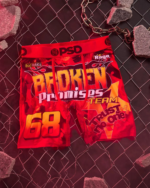 Red pouch keychain with "Broken Promises" text and graphics, attached to metal chain against chain-link background.