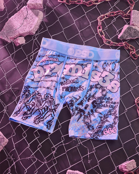 Blue and pink graphic print boxer briefs with "Broken Promises" text and skull imagery, displayed on dark mesh background.