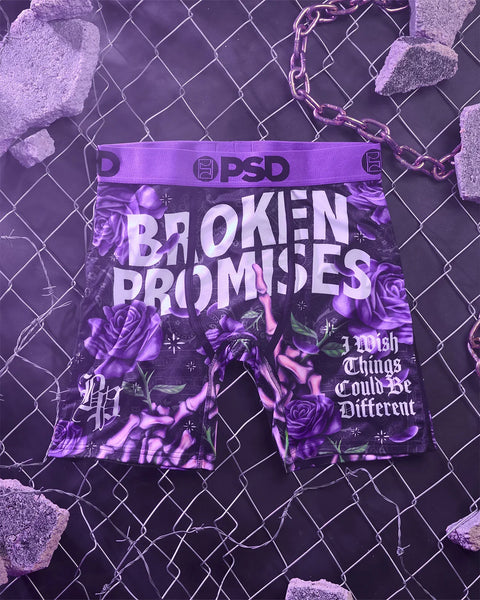 PSD purple boxer briefs with "Broken Promises" text and rose graphic design, displayed against chain-link fence background.