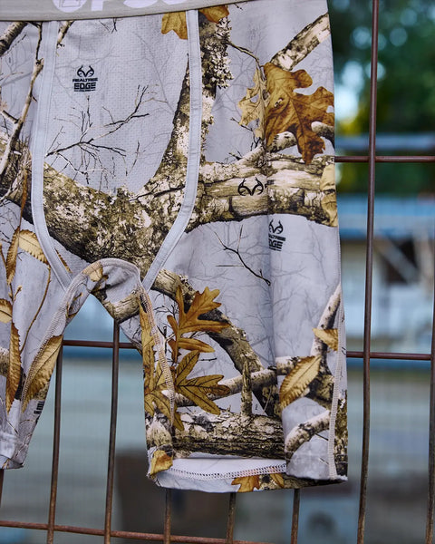 Realtree Edge grey camouflage fabric with birch trees, branches, and golden leaves printed throughout.