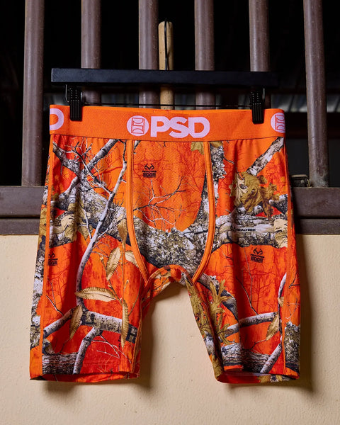 Orange Realtree Edge camo boxer briefs with PSD waistband displayed on hanger.