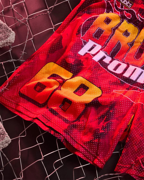 Red active short with yellow and pink graphic design and perforated mesh panels, displayed flat on geometric background.