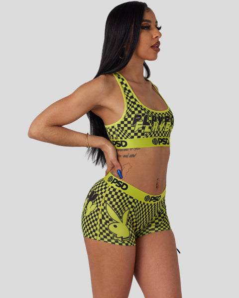 Woman wearing neon yellow and black checkered Playboy sports bra and shorts set with bunny logo.