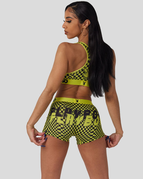 Woman wearing lime green and black checkered sports bra and shorts set with Playboy branding, shown from back.