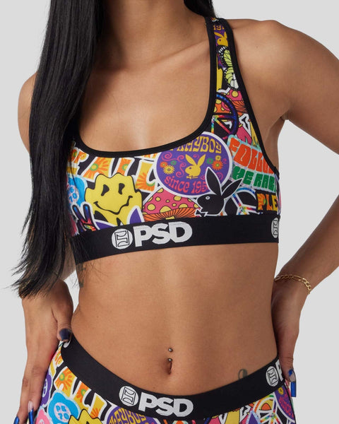Colorful Playboy-branded sports bra with yellow smiley face, peace symbols, and multicolored graphic print on black elastic b