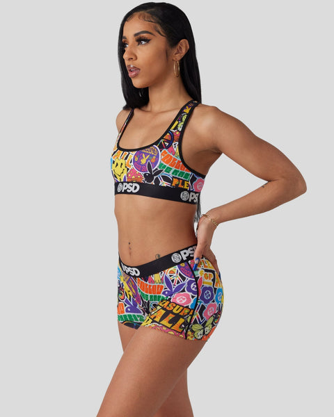 Woman wearing colorful Playboy-branded sports bra and shorts with multicolored peace symbol and graphic print design.
