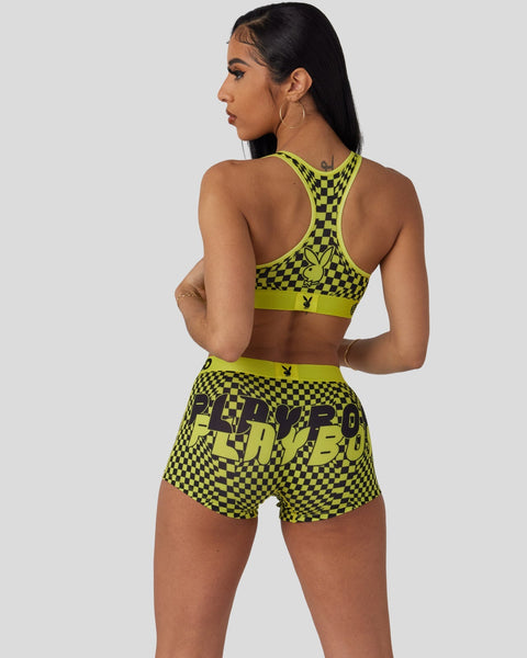 Woman wearing neon yellow and black checkered sports bra and shorts set with Playboy branding, shown from back view.