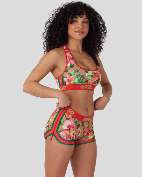 Woman wearing red sports bra and shorts with pink and green floral print and red trim.