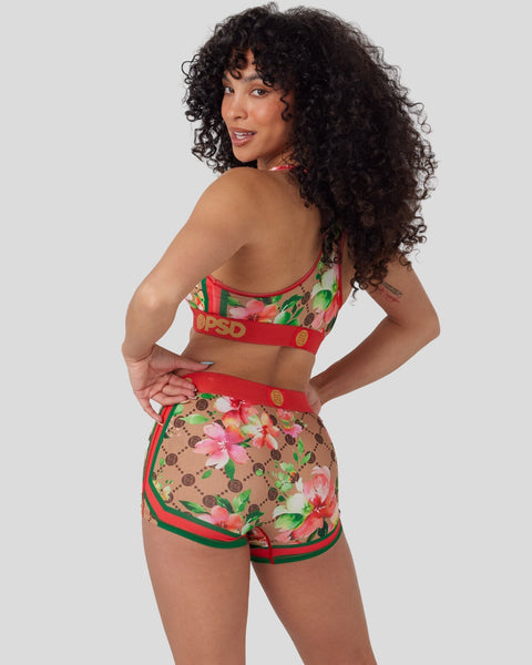 Woman wearing red and tan floral print sports bra and shorts set with green and red trim.