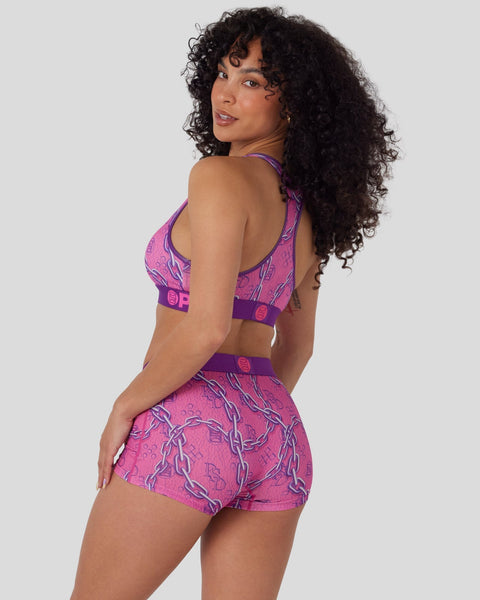 Woman wearing pink and purple patterned sports bra and matching shorts with chain graphic design.