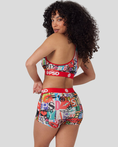 Woman wearing red sports bra and matching shorts with colorful abstract text print design, shown from back.