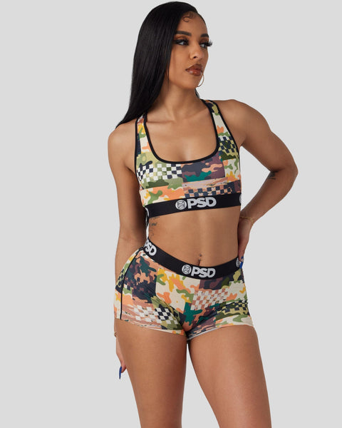 Woman wearing multicolored patterned sports bra and matching shorts with black waistbands and branding.