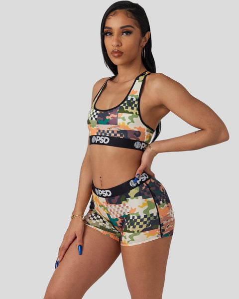 Woman wearing multicolor patchwork sports bra and matching shorts with PSD branding and geometric patterns.