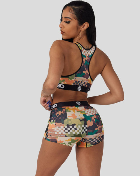 Woman wearing camouflage and checkered patterned sports bra and shorts set with black trim and branding.