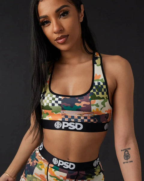 Patterned sports bra with black PSD waistband, featuring camouflage and checkered design elements in orange, green, and cream