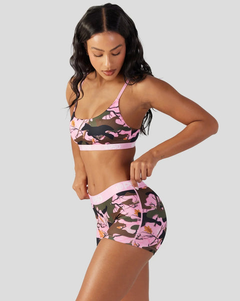 Woman wearing pink and olive camo sports bra and shorts set with matching trim.