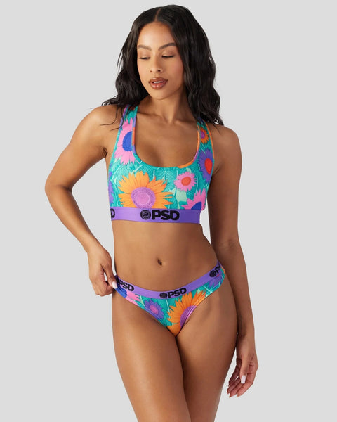 Woman wearing colorful sunflower-print sports bra and matching briefs with purple PSD branding on turquoise background.