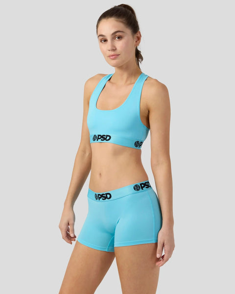 Woman wearing bright turquoise sports bra and matching boy shorts with PSD branding.