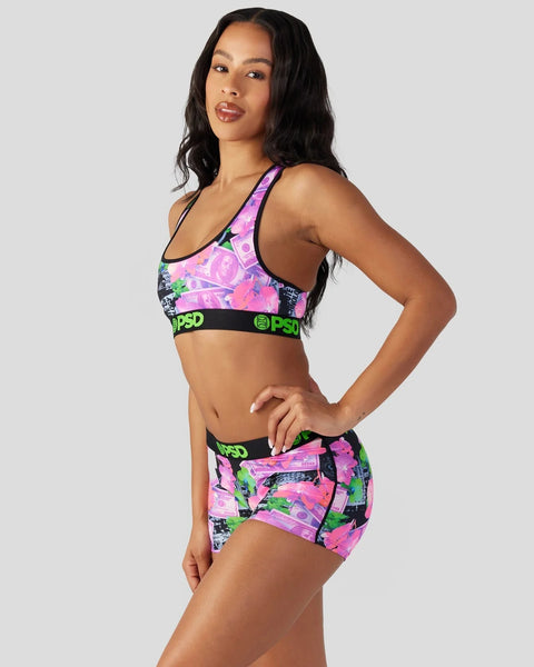 Woman wearing pink, purple, and neon green patterned sports bra and shorts set with black elastic waistband.
