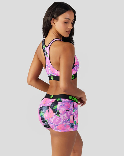 Woman wearing pink, purple, and black floral sports bra and matching shorts with green text bands.