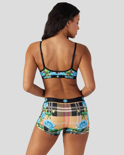 Woman wearing tartan and floral patterned sports bra and shorts set with black straps and waistbands.