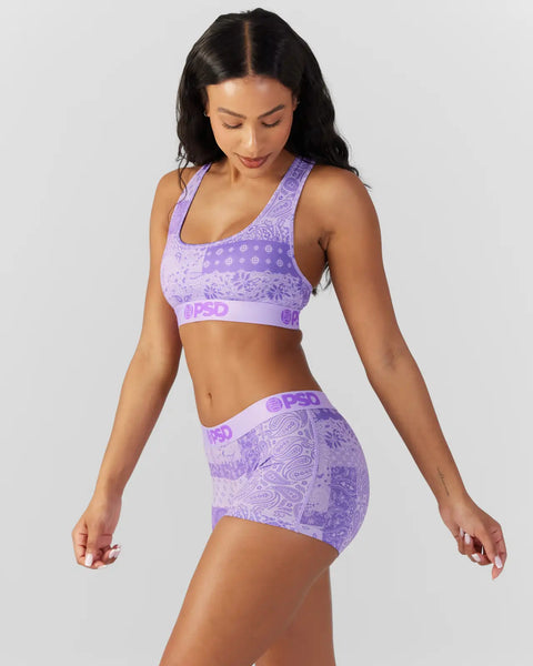 Woman wearing purple patterned sports bra and matching shorts with bandana-style design and branding.