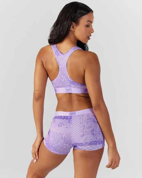 Woman wearing a purple paisley patterned sports bra and matching shorts set, shown from behind.