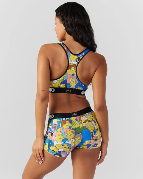 Woman wearing Simpsons character print sports bra and shorts set with blue and multicolored background, shown from back view.